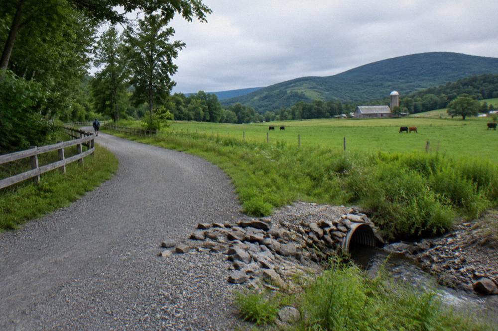 A wide compacted stone rail trail curving through green Vermont farmland