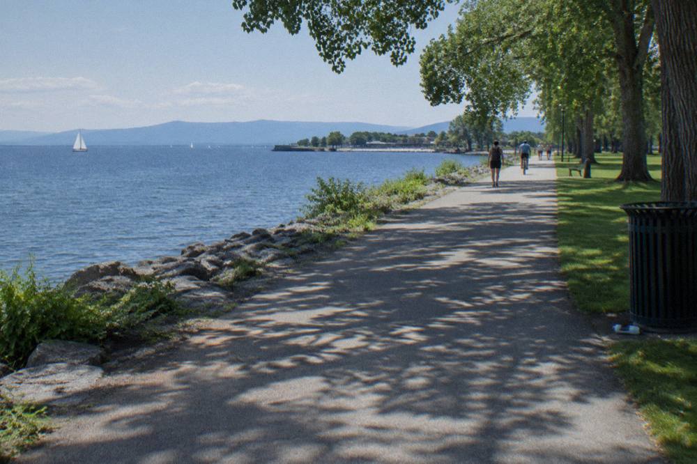 Wide paved bike path along the Burlington waterfront with lake and distant mountains beyond