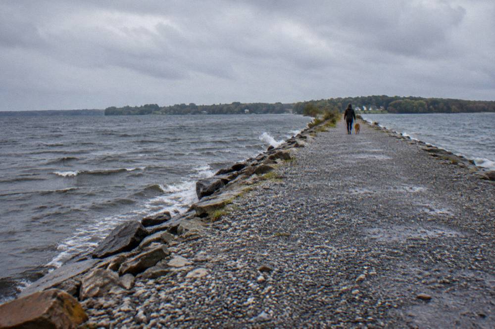 Narrow gravel causeway path crossing open water with distant island shoreline