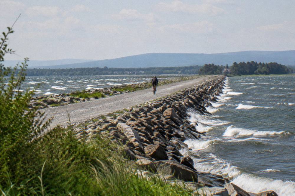 A cyclist riding a gravel causeway trail with open water on both sides