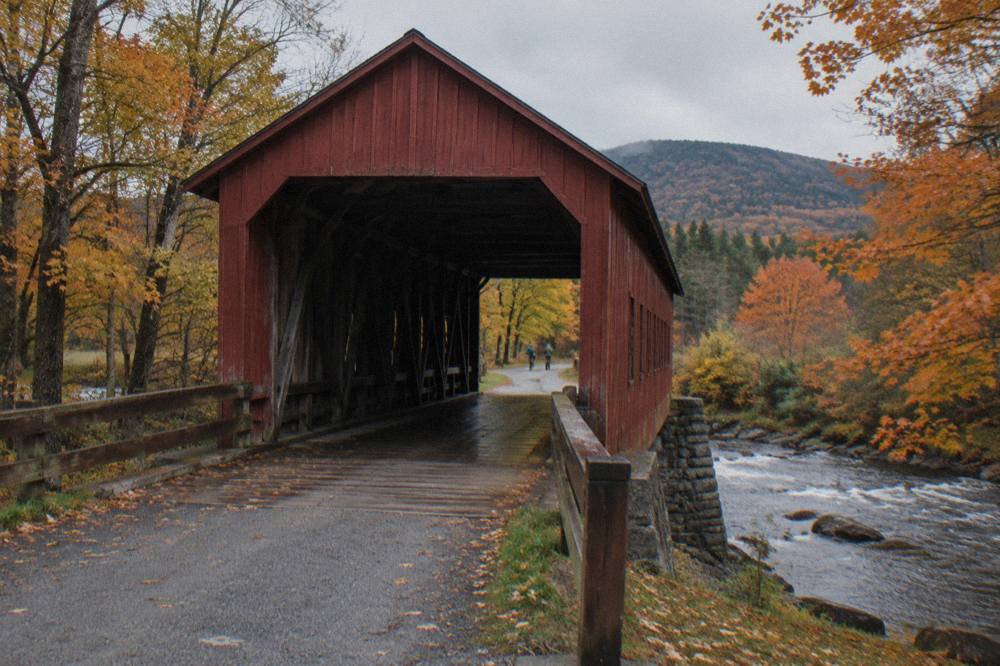 A covered bridge on a rural Vermont road with fading orange maples on both sides
