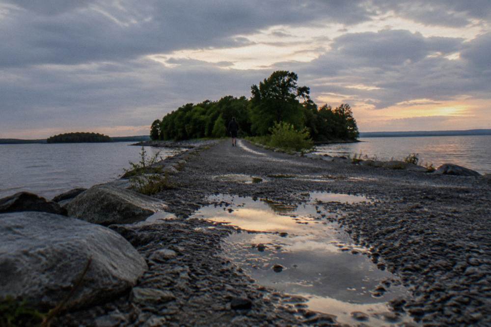 A narrow gravel trail stretching across open water toward tree covered islands on the horizon
