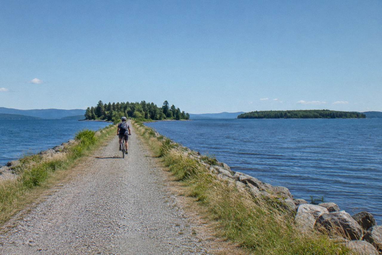 Cyclist on a granite causeway crossing Lake Champlain near Colchester, green islands on the horizon
