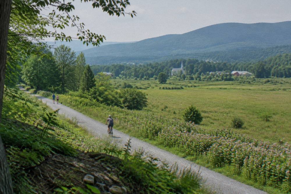 A wide crushed stone trail crossing an open field toward a line of Vermont hills