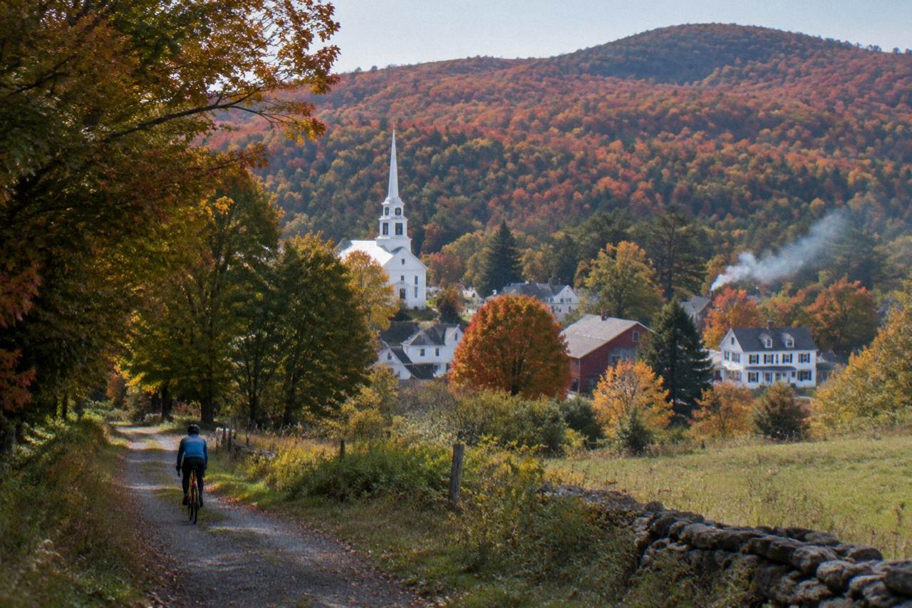 The white steepled village of Woodstock in its valley under red and orange autumn hills, chimney smoke drifting
