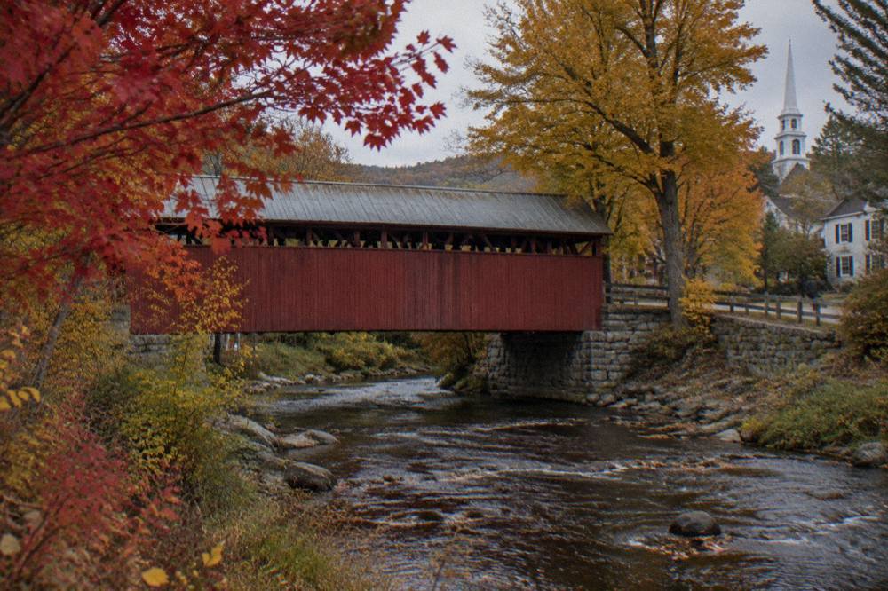 A covered bridge over a stream surrounded by red and gold trees