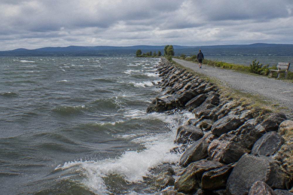 Narrow gravel trail crossing open water with lake on both sides