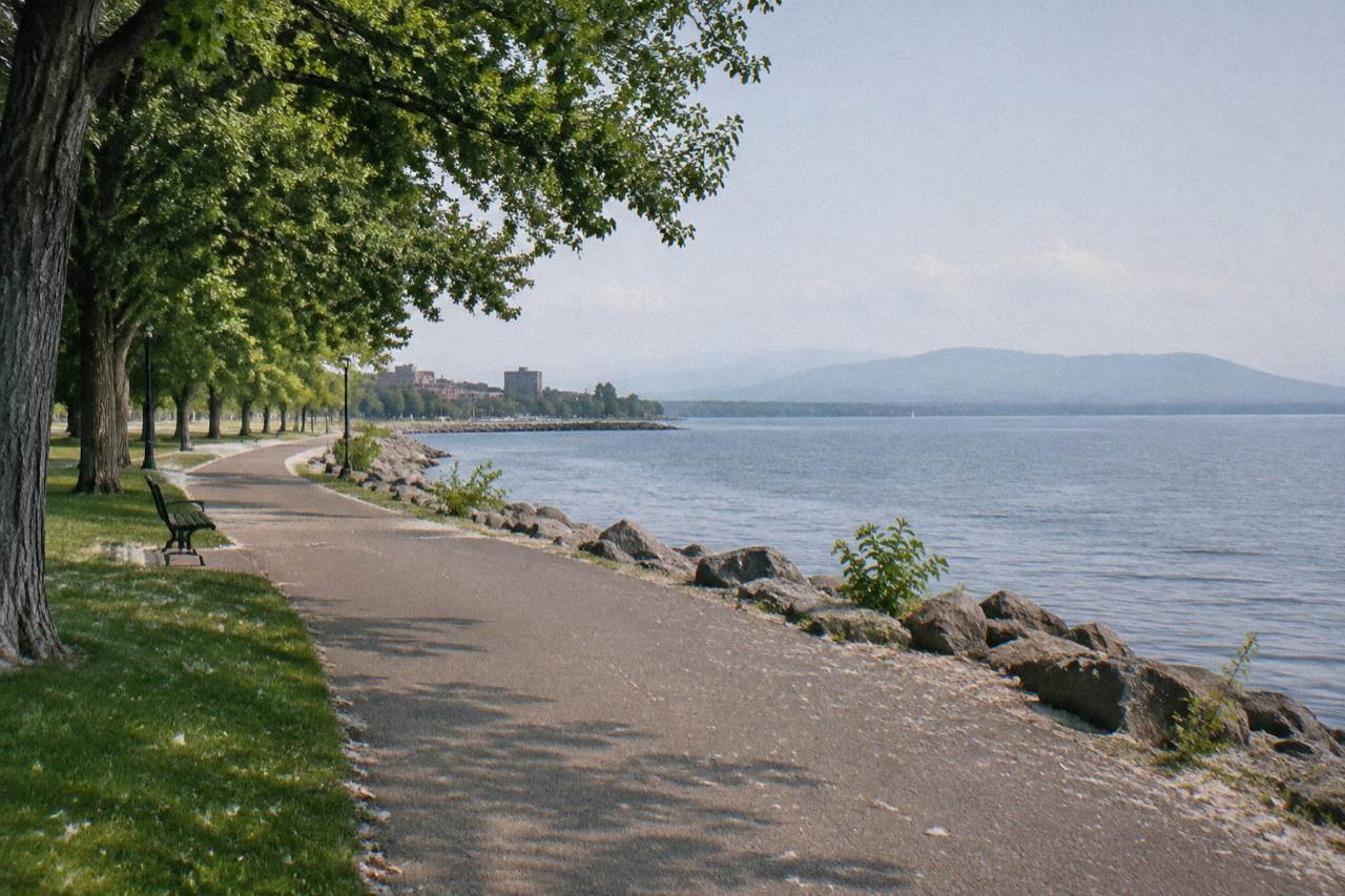 Empty paved bike path along a lake shoreline with green hills behind it