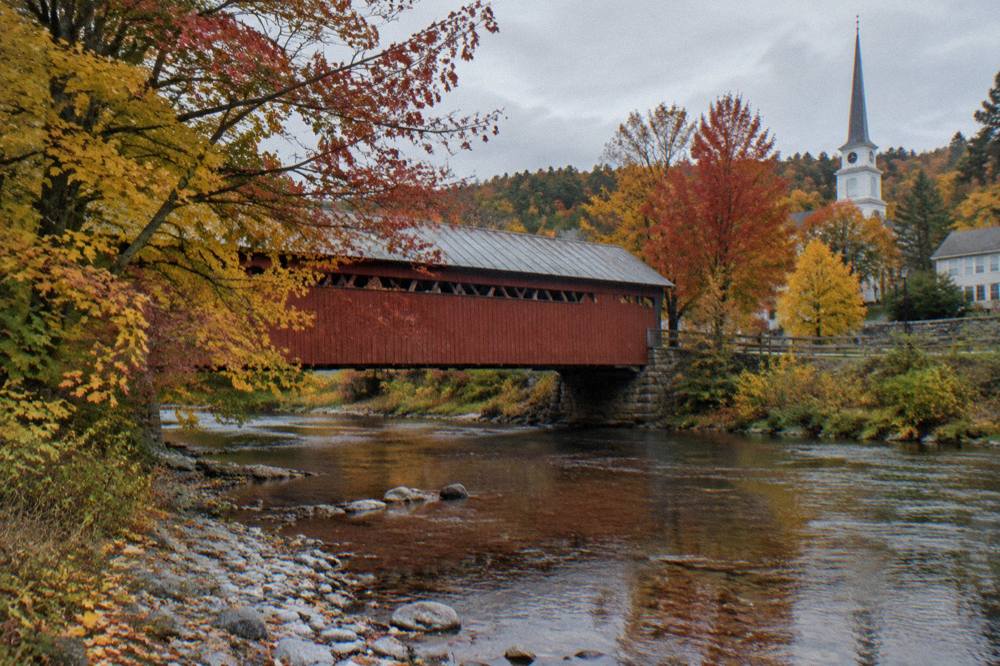 A covered bridge over a stream surrounded by red and gold maple trees
