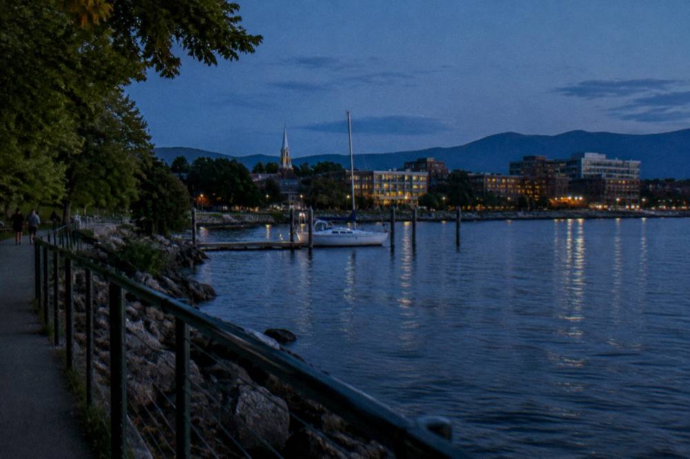 Evening view over a lakefront city skyline from a paved path with a railing in the foreground