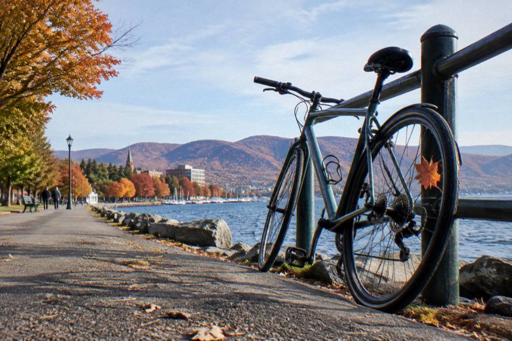 Bicycle leaning against a railing beside a lake with hills across the water in autumn color