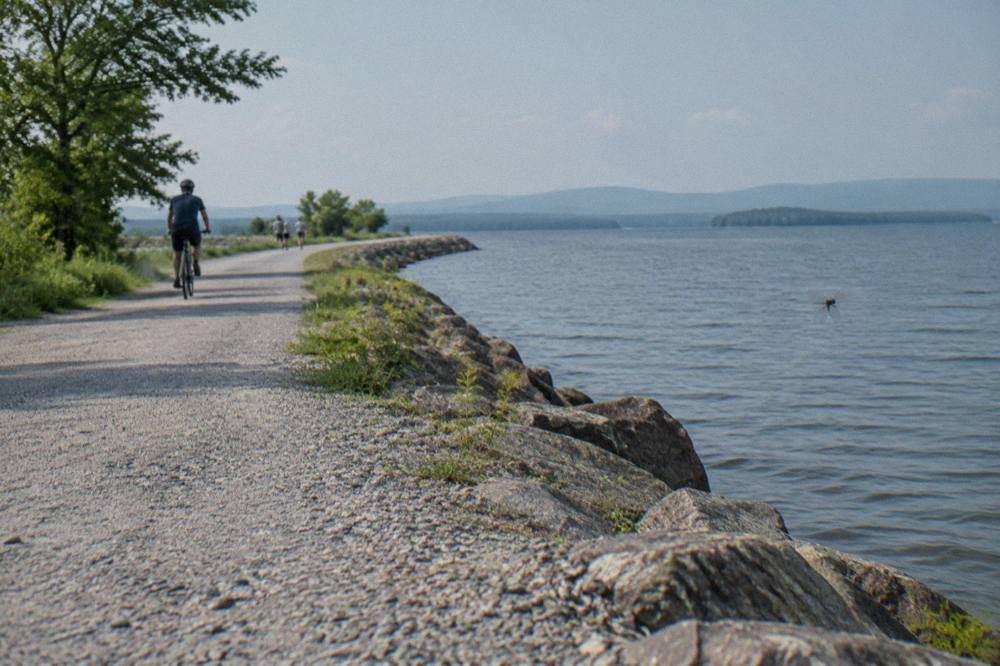 A paved lakeside bike path curving beside open water with tree covered hills beyond