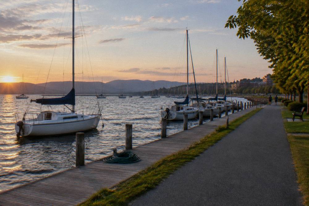 A lakeside boardwalk with moored sailboats and a paved path running beside the water
