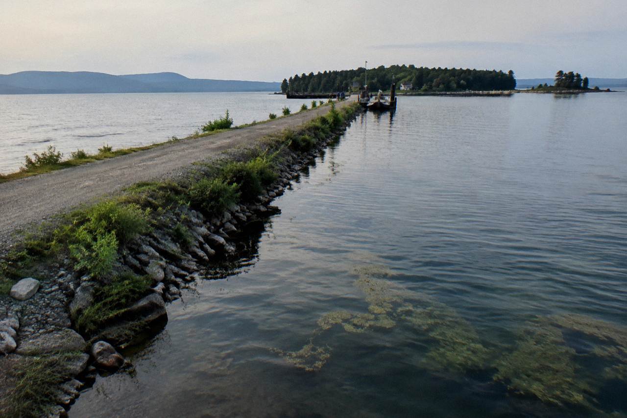 A gravel bike trail crossing a narrow causeway over open lake water with distant hills