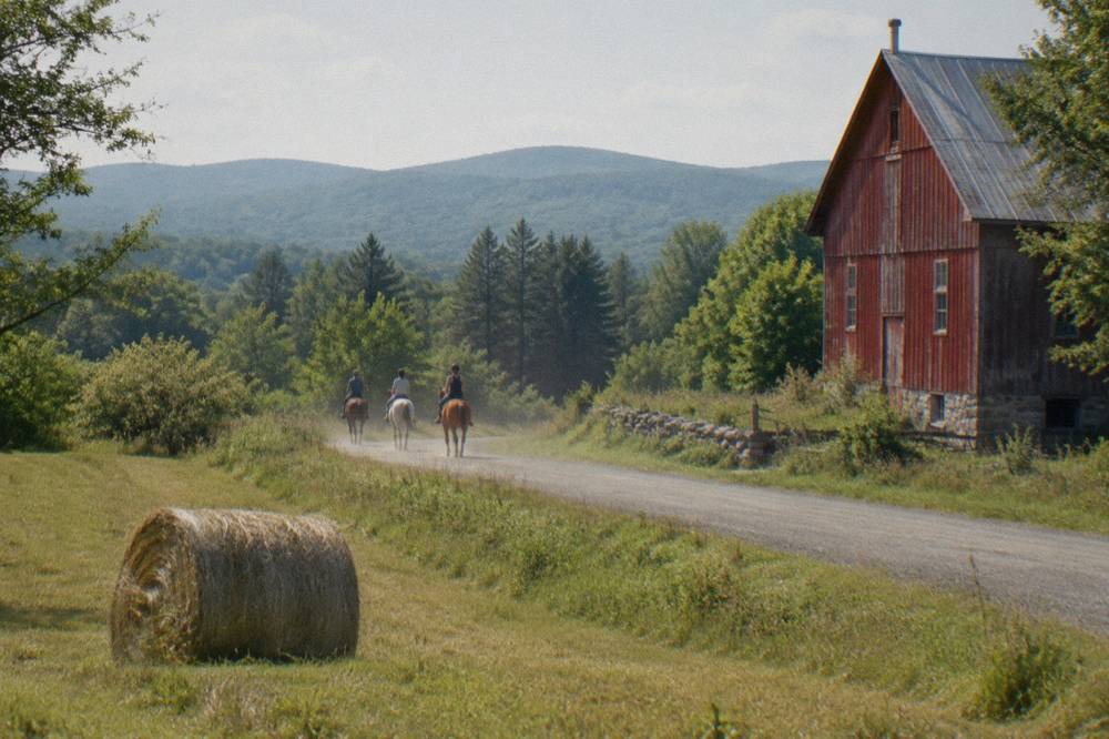 Small group of cyclists spread along a quiet country road past a red barn