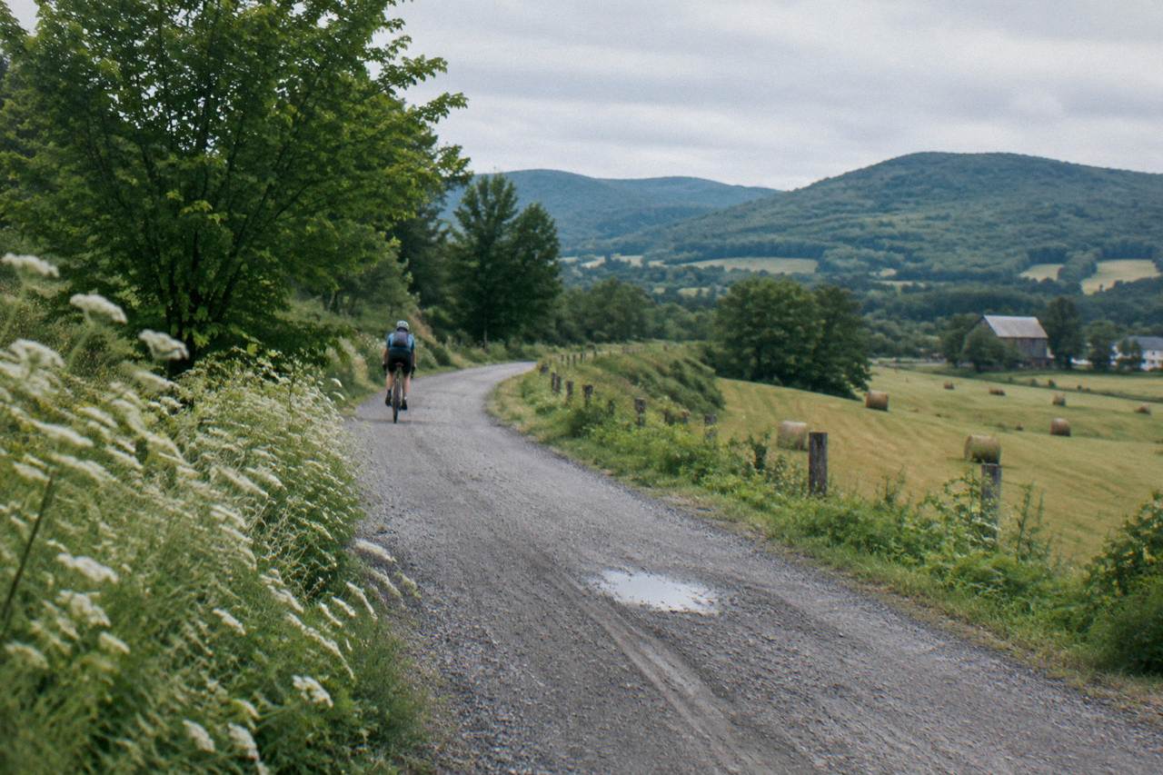Empty paved rail trail curving through green Vermont hills with farmland on both sides