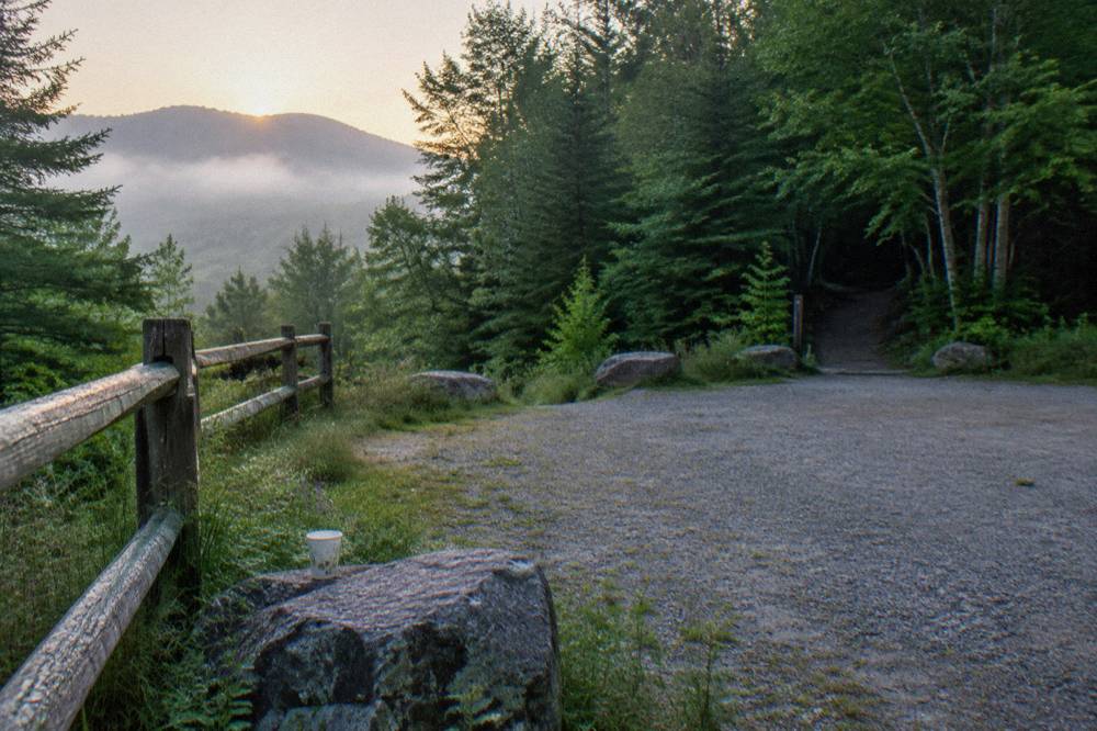 A gravel parking area beside a wooded trailhead