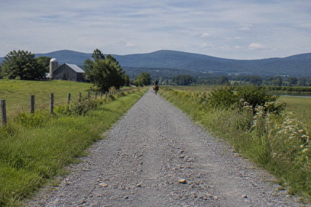 A packed crushed stone trail stretching straight through open farmland toward distant hills