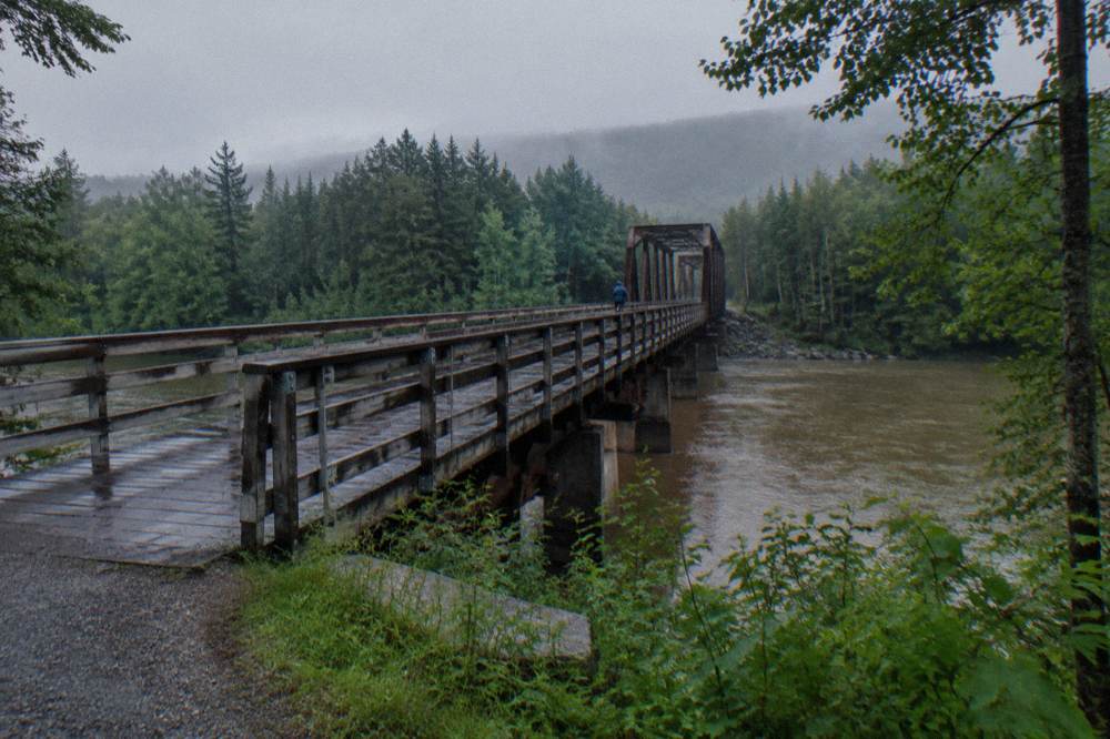 A rail trail crossing a river on a long narrow bridge with forest on both banks