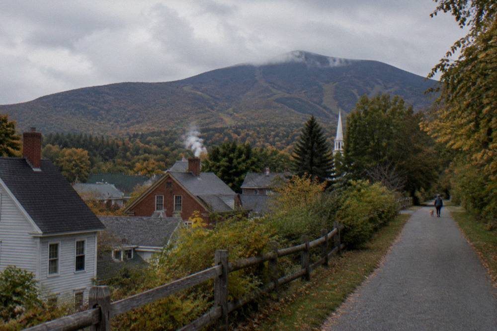 A quiet Vermont village street with forested mountains rising behind the rooftops