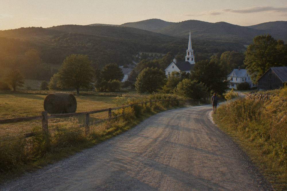 A gravel road curving through open farmland with wooded hills in the distance