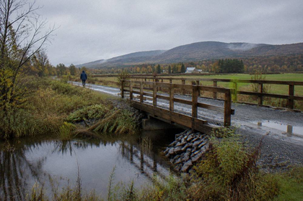 A rail trail of compacted crushed stone crossing open countryside with hills beyond
