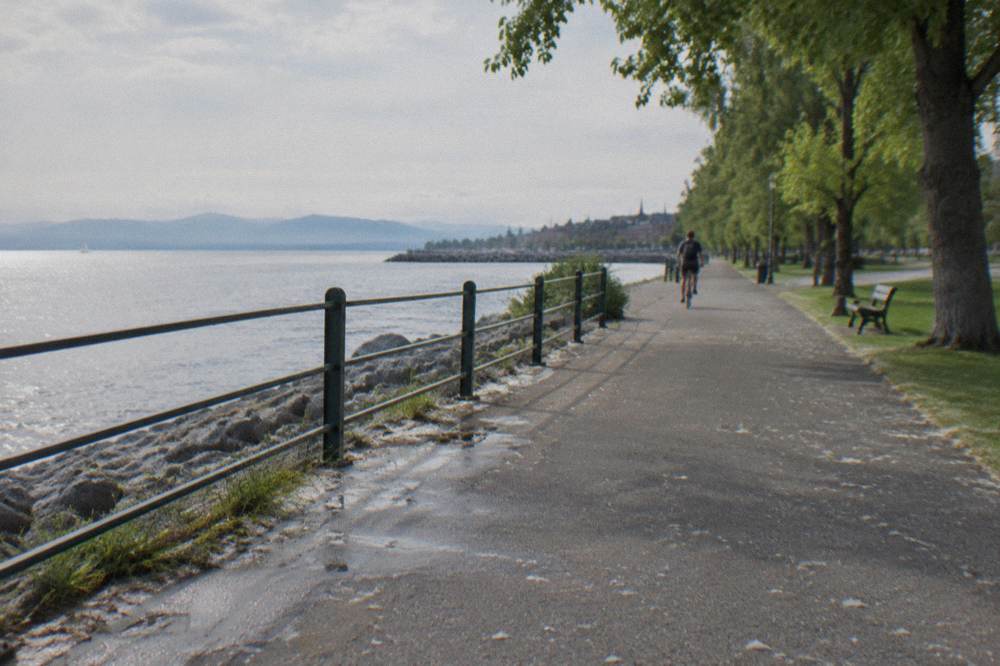 A cyclist pedaling an e-bike along a wide multi use path beside a lake