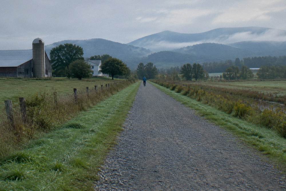 A long crushed-stone rail trail stretching straight through open farmland toward distant hills