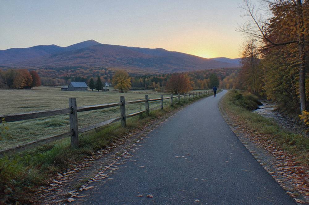 An empty paved country road curving through rolling farmland with hills beyond