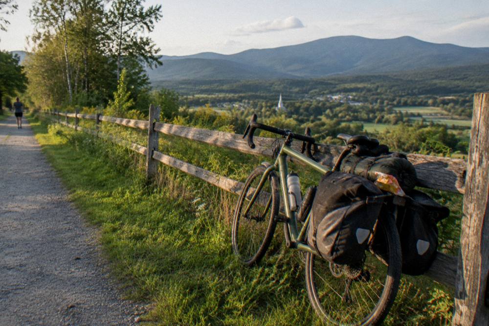 A bicycle leaned against a wooden fence with saddlebags attached and hills in the distance