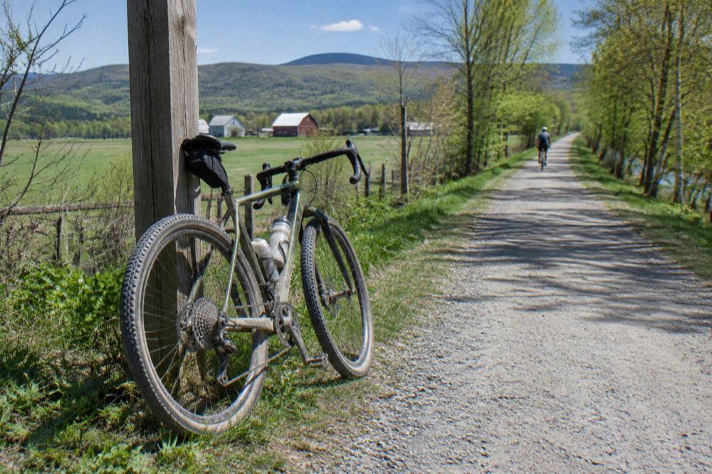 A gravel bike leaning on a stone dust rail trail beside farmland