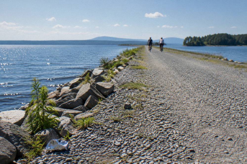Cyclists riding a paved lakeside bike path with water on one side