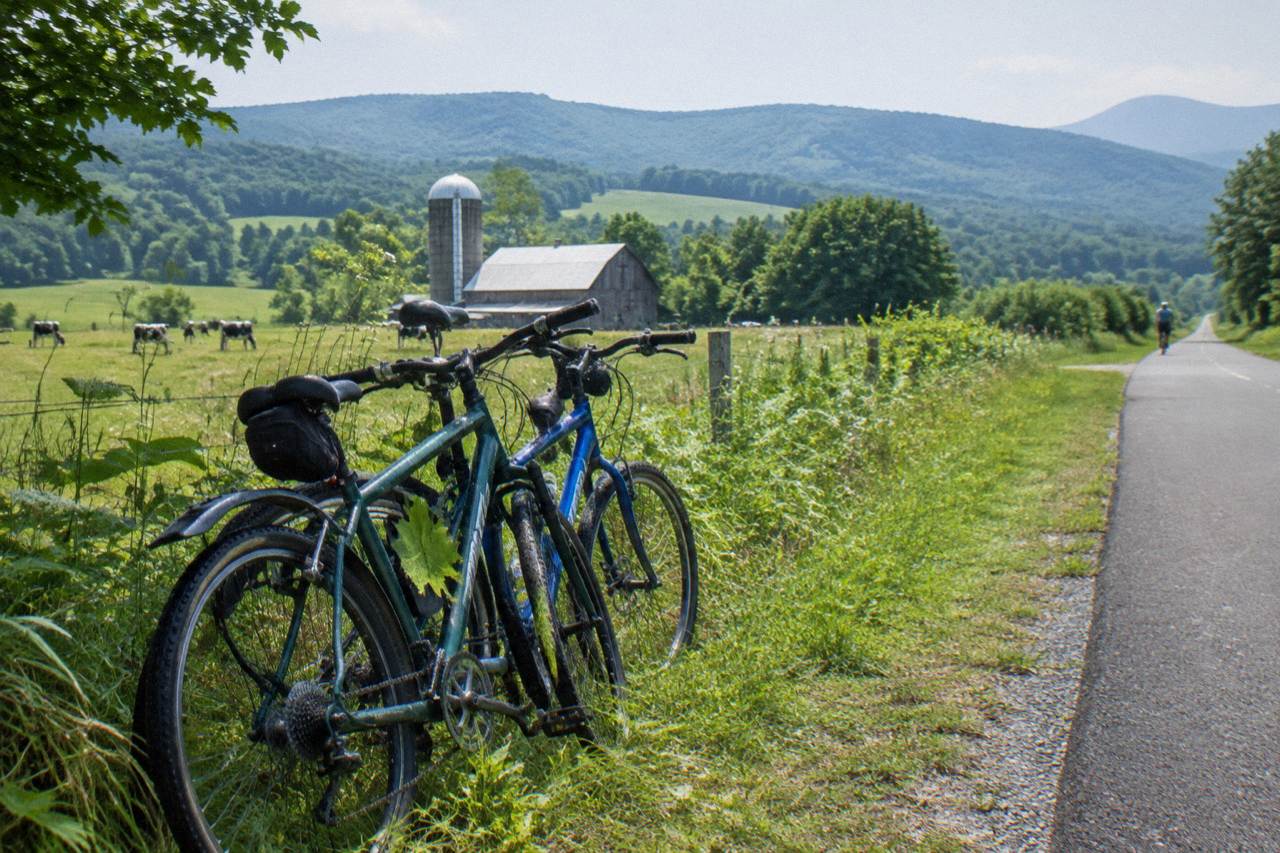 Two bicycles parked beside a quiet Vermont country road with green hills behind them