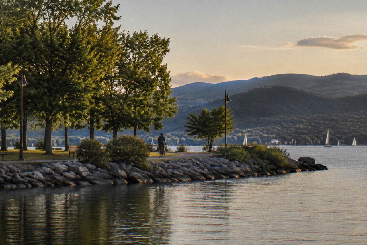 A quiet paved bike path beside a lake with tree-covered hills in the distance