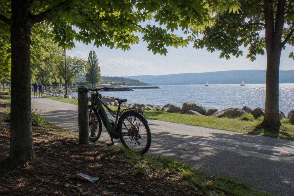 A pedal assist electric bike leaning against a post beside a paved lakeside bike path