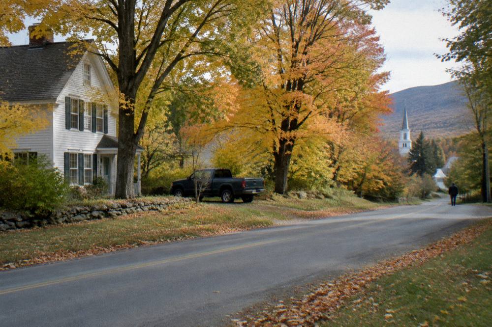 A quiet paved country road with no shoulder winding between maple trees in Vermont