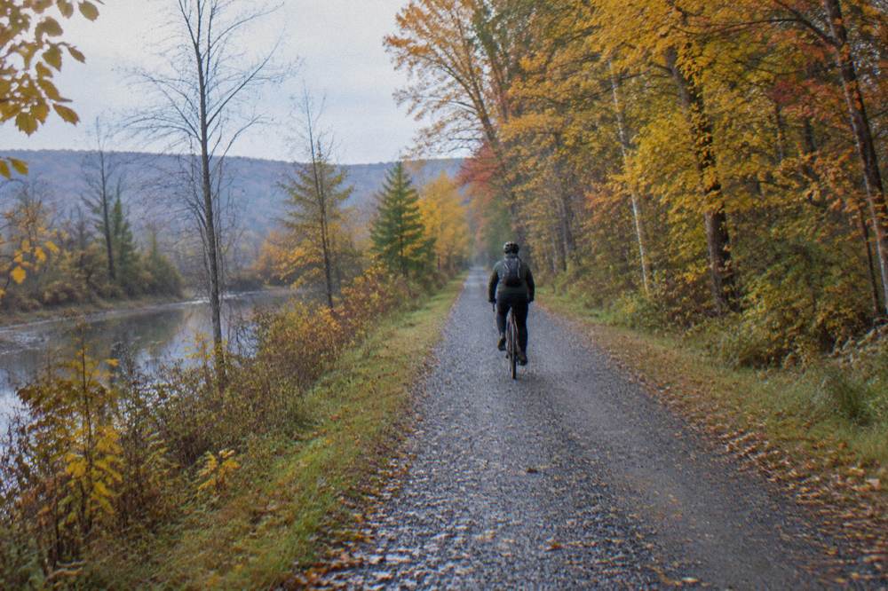 A cyclist on a compacted stone rail trail passing through yellow and orange forest in Vermont