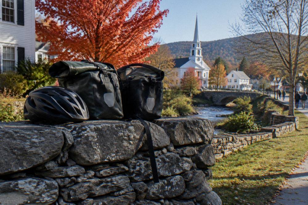 A loaded touring bicycle parked beside a stone wall with red maple foliage behind it