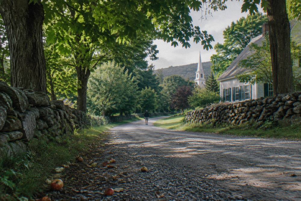 A packed gravel road winding between stone walls and maple trees in Vermont